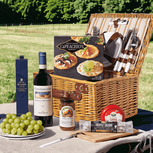Tuscan CastelGiocondo Red Wine Picnic Basket from Monthly Sommelier. This gift includes a bottle of CastelGiocondo Brunello di Montalcino, fresh green grapes, sweet marmalade, gouda cheese, truffle salami, an assortment of crackers, dark chocolate truffles, a small cutting board, and a wonderful picnic basket with all the necessary cutlery and dishware.